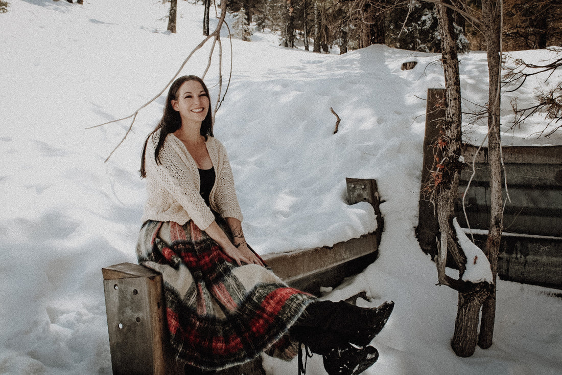 Smiling Woman Sits on a Fence in a Snowy Woods